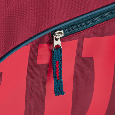 A vibrant red bag with a blue zipper is partially open showcasing a zipper pull. The context suggests it is likely used for carrying items or sports equipment.