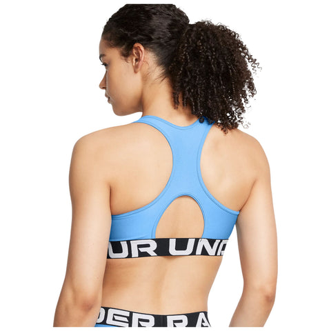 Female figure wearing a blue sports bra stands with her back to the viewer showcasing a racerback design and a black Under Armour logo band around her waist in a neutral background.