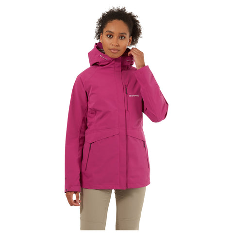 A woman is adjusting her hair while wearing a bright pink waterproof jacket with a hood in a neutral white background, suggesting a focus on outdoor apparel.