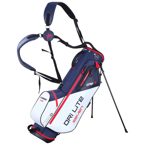 A golf carry bag stands upright with three supporting legs extended the bag features a navy blue and white design with red accents and adjustable shoulder straps for easy transport