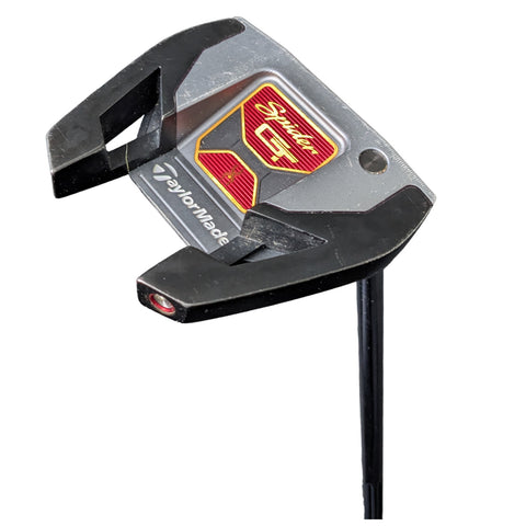 A golf putter is positioned upright showcasing its head featuring a silver and black design with a red and gold logo indicating the brand TaylorMade with the model name Spindle GT displayed prominently.