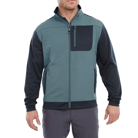 A man stands wearing a stylish zippered jacket featuring a teal body with a dark blue textured sleeve and pocket design in a neutral setting.