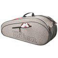 A grey tennis bag with the logo Wilson sits on a flat surface showcasing its rounded shape and multiple compartments one pocket displays a tennis ball and a white sock.