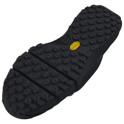 A black shoe sole with a textured surface and raised patterns is positioned flat. The sole is designed for grip and durability in outdoor settings. A yellow label is visible on the sole.