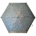 A blue floral-patterned umbrella is opened wide displaying small white and orange flowers against a light blue background in a neutral setting.