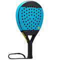 A blue and black paddle with a perforated surface is displayed upright. It features a textured grip handle and a wrist strap, designed for sports like padel or tennis. The brand name "Wilson" is visible.