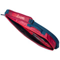 A red sports bag is open displaying secured equipment inside with straps and a buckle visible the bag is suitable for carrying sports gear or accessories.