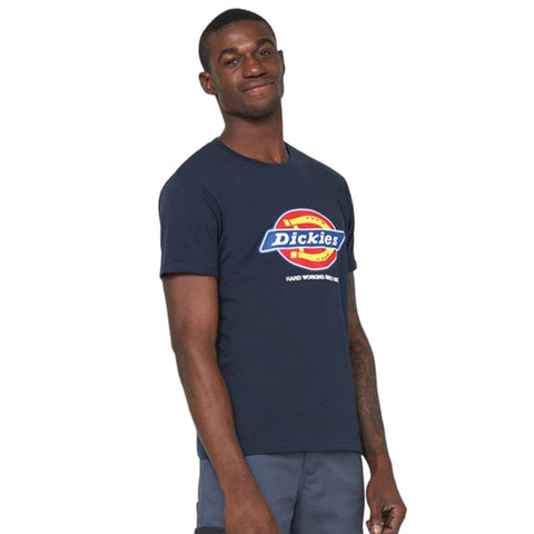 A person stands confidently wearing a dark blue t-shirt with a colorful Dickies logo and the words "HARD WORKING MATERIAL" displayed beneath it, set against a plain background.