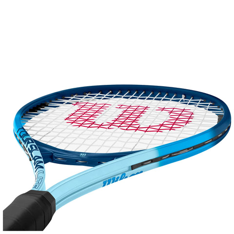 A blue tennis racket with a black handle rests in a slightly angled position showcasing a white string pattern and a prominent red logo on the strings indicating the brand.