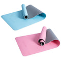 Two yoga mats are displayed side by side one is blue with a grey underside and the other is pink with a grey underside both are slightly rolled at one end and laid flat on a surface.