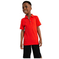 A boy wearing a bright red polo shirt and black shorts stands smiling with a relaxed posture in front of a plain white background showcasing casual attire.