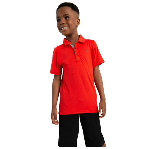 A boy wearing a bright red polo shirt and black shorts stands smiling with a relaxed posture in front of a plain white background showcasing casual attire.