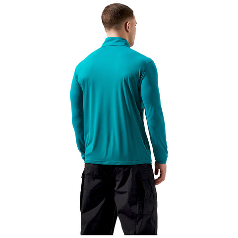 A person wearing a teal long-sleeve shirt is standing with their back facing the viewer in a neutral environment. The individual has short hair and is dressed in black pants.