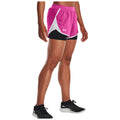 A pair of athletic shorts in bright pink with black underlayers is showcased on a model standing confidently in black running shoes in a neutral background.