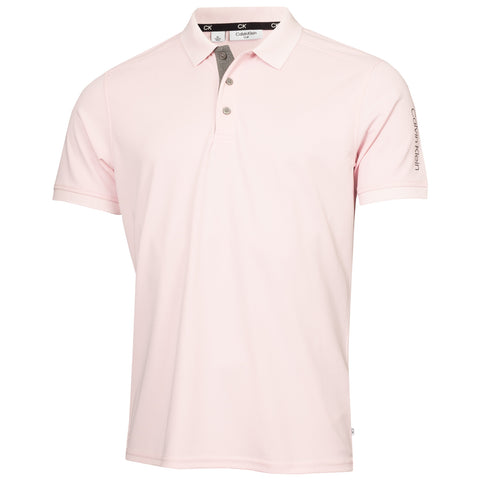 A pink polo shirt hangs with a folded collar and three buttons showcasing its soft fabric and short sleeves displayed against a neutral background. The brand name Calvin Klein is visible on the collar.