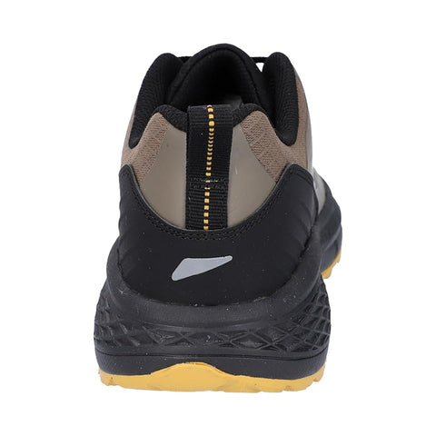 A sneaker is positioned upright showcasing its rear design it features a black and gray color scheme with a textured sole and a yellow accent on the bottom