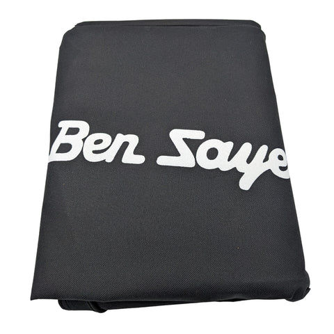 A rectangular, gray golf bag cover lies flat on a surface displaying the text "Ben Sayers" in white, indicating it is designed to protect and cover a golf bag during transport or storage.