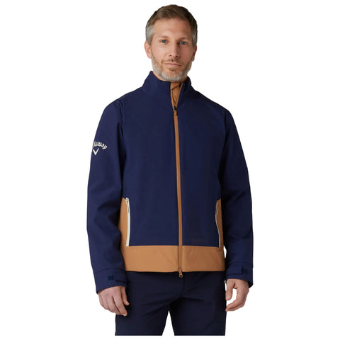 A man stands wearing a navy and brown jacket with a zipper and side pockets presenting a stylish design in a neutral background perfect for outdoor activities.