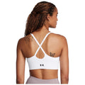 A person is wearing a white sports bra with crisscross straps showcasing a butterfly tattoo on their back in a neutral setting.