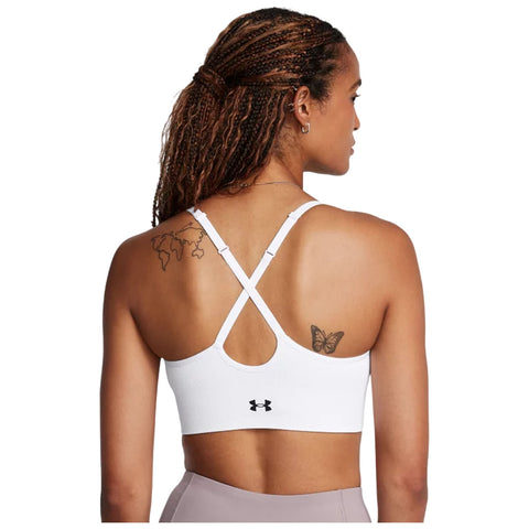 A person is wearing a white sports bra with crisscross straps showcasing a butterfly tattoo on their back in a neutral setting.