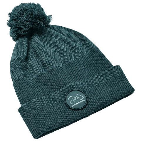 A green knit beanie with a pom pom on top and a snug folded cuff features an embroidered Under Armour logo on the front showcasing a stylish winter accessory.