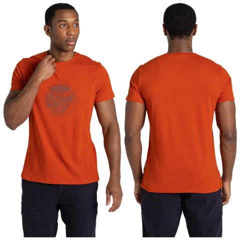 A man wears an orange t-shirt while adjusting it. The shirt features a graphic design on the front. He is in a neutral setting with no distinct background elements.