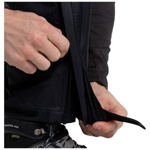 A hand is grasping the zipper of a black jacket while partially opening it. The context includes a textured black fabric and a rugged hiking boot with laces visible.