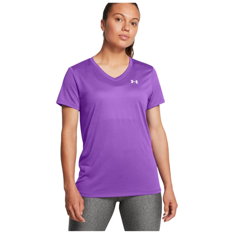 A woman is standing in a purple athletic t-shirt and gray workout leggings looking confidently at the viewer. The background is plain, emphasizing her attire.