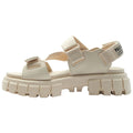 A light beige sandal features thick rubber soles and an open design with adjustable straps across the foot. It is presented against a white background, emphasizing its modern style.