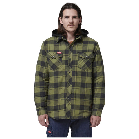 A man stands wearing a green and black plaid flannel shirt with a hood and two chest pockets while holding his left hand with a relaxed expression against a plain white background.