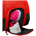 A red bag with a zippered compartment is opened revealing a pair of athletic shoes with pink and white detailing resting inside on a black fabric lining.