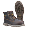 A brown safety boot with yellow logo stands upright next to a sole showing a tread pattern designed for grip and oil resistance in a plain background setting.