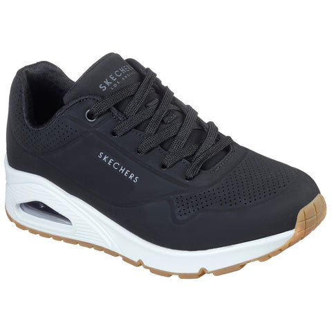 Black Skechers sneakers with a smooth upper and perforated design sit prominently displaying air cushioning in the sole against a neutral background suggesting a casual footwear choice.