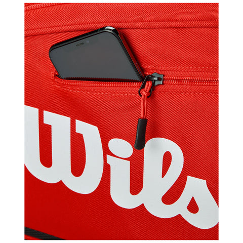 A red bag features a partially visible black smartphone in a zipped pocket while displaying the word "Wils" in white lettering on its surface.