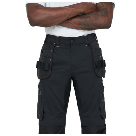 Black cargo pants with multiple side pockets are being worn by a person standing with arms crossed in a neutral environment. The pants feature belt loops and light stitching details.