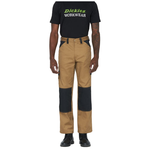 A person stands wearing a black t-shirt with "Dickies WORKWEAR" printed on it and tan work pants with black knee patches and side pockets, paired with black boots.