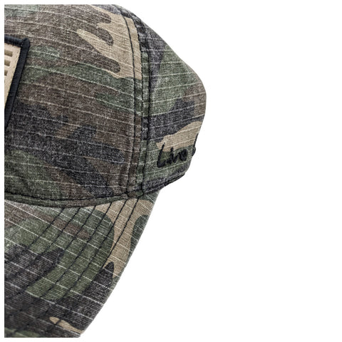 A camouflaged baseball cap displays intricate stitching and a logo on the front panel while lying in a neutral background highlighting its textured fabric and design details.