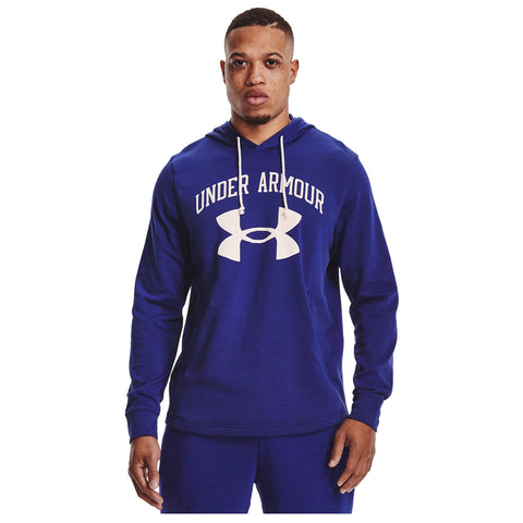 A person is standing wearing a blue hooded sweatshirt with "UNDER ARMOUR" printed in white across the chest against a plain background. The individual appears focused.