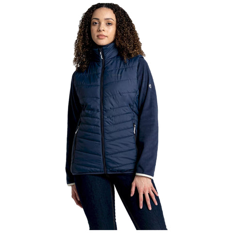 A woman wears a navy blue insulated jacket with a high collar and a zipper in a neutral background standing calmly while her hand rests lightly on her thigh.