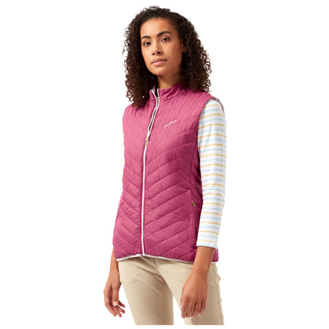 A woman stands confidently wearing a pink quilted vest over a striped long-sleeve shirt. The background is plain and light, emphasizing her outfit and expression.