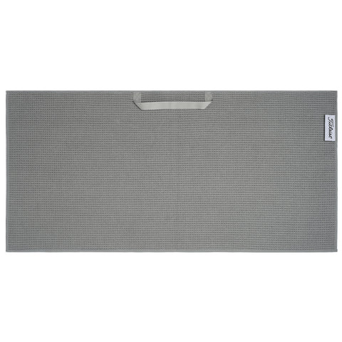 A gray textured mat with a handle is displayed flat on a surface featuring a subtle pattern and a logo on one corner indicating the brand is Titleist