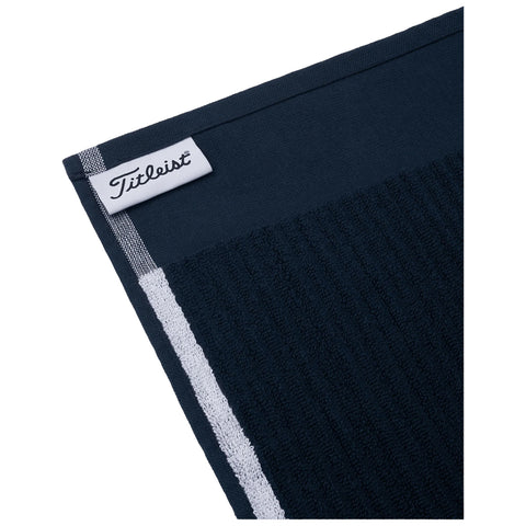 A dark blue golf towel with a textured section is displayed at an angle the towel has a white logo tag labeled Titleist and a white striped edge