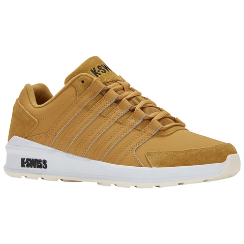 A tan sneaker with a smooth surface and textured accents sits on a flat surface showcasing its white sole and laces while displaying the brand logo K-Swiss on the tongue and side.