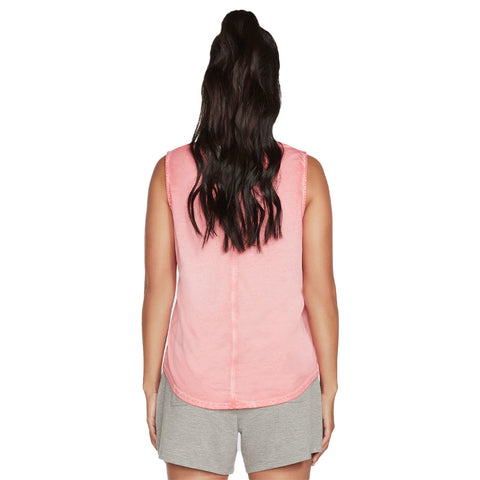 A person with long dark hair is viewed from the back wearing a pink sleeveless top and gray shorts standing in a neutral background with no distractions.