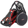 A compact red and black folding golf trolley is shown in a stacked position with a carrying strap attached it appears ready for transport in a casual indoor setting.