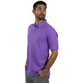 A man wears a purple polo shirt and light gray pants standing with a slight turn towards his left looking off into the distance against a plain white background.