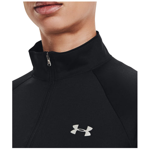 A person wears a black zip-up athletic jacket with a high collar featuring a silver logo on the left side the focus is on the upper torso and neck area.