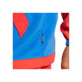 A colorful jacket featuring bright blue fabric and red accents showcases a small embroidered label with stripes on the side while a hand is visible holding the arm.