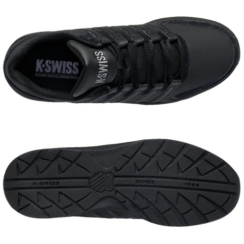 A black sneaker featuring a textured upper with laces and branding on the tongue rests on a flat surface showing its detailed tread pattern on the sole.