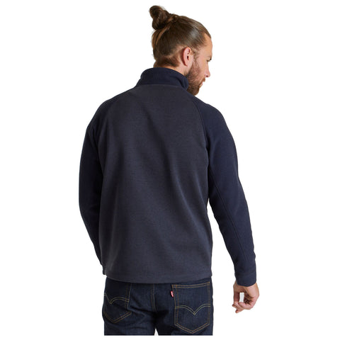 A man stands with his back to the viewer wearing a dark-colored fleece jacket and jeans in a plain white background setting